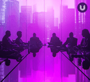 The silhouettes of a group of 9 figures sit at a table in a conference room with floor to ceiling windows overlooking a skyline of skyscrapers at sunset