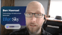A bald man with a beard and glasses, wearing a black shirt, in an office with a window and a hat on the window sill. There's a graphic overlay with the name 'Ben Haensel,' his title 'Technology Infrastructure Specialist,' and the logos of 'Blue Sky Studios' and 'USERWAY.