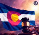 A Colorado flag waves in front of a sunset; a gavel on a sounding block rests in front of the flag