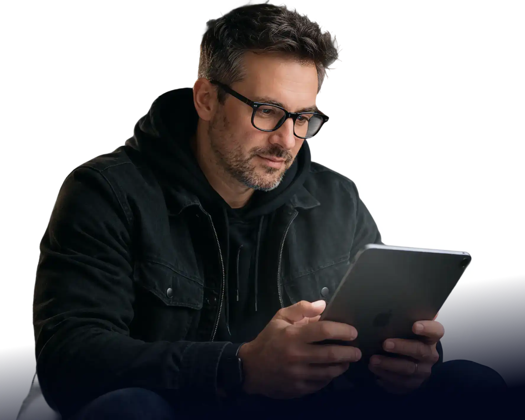Person wearing glasses and a dark jacket, looking down at and holding a tablet.
